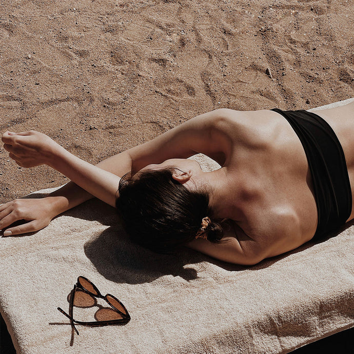 POST BEZAU JUICE Summer PackageFrau am Strand auf Handtuch liegend mit Sonnenbrille
