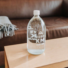 Load image into Gallery viewer, Mit Wasser gefüllte Hotel Post Bezau Glasflasche ZERO KM WATER 1 l auf einem Tisch vor einem Sofa
