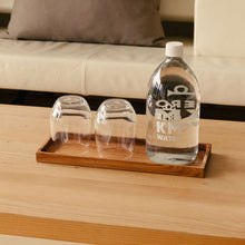 Load image into Gallery viewer, Mit Wasser gefüllte Hotel Post Bezau Glasflasche ZERO KM WATER 1 l auf dem Hotel Post Bezau Holzbrett mit zwei leeren Wassergläsern auf einem Tisch vor einem Sofa
